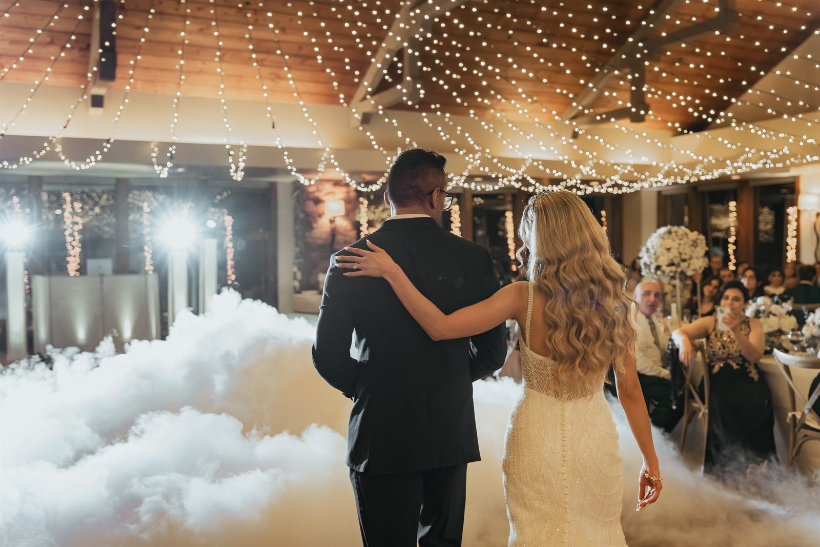 Bride and groom walking onto a fog-covered dance floor beneath a canopy of string lights