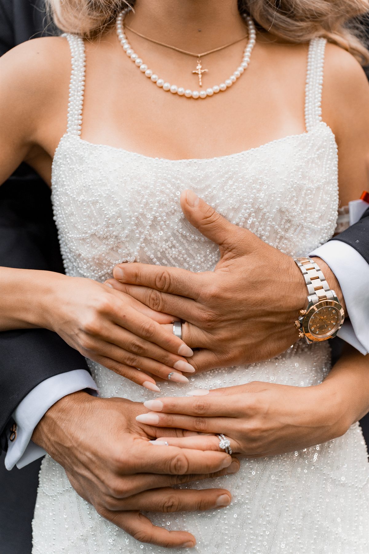 Close-up of the couple's hands and rings as the groom embraces the bride in her beaded gown