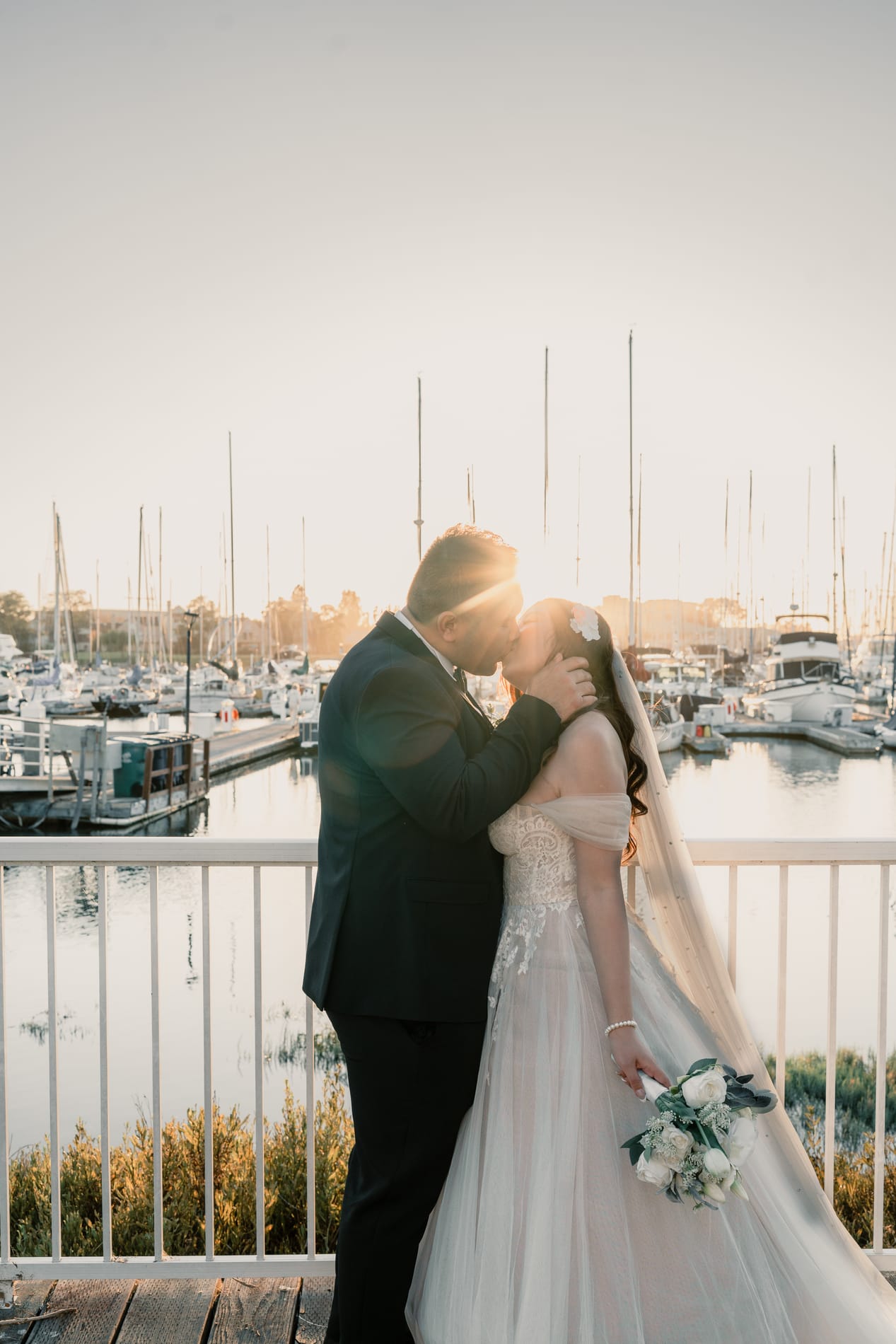 Bride and groom kissing on the marina boardwalk as the sun breaks between them
