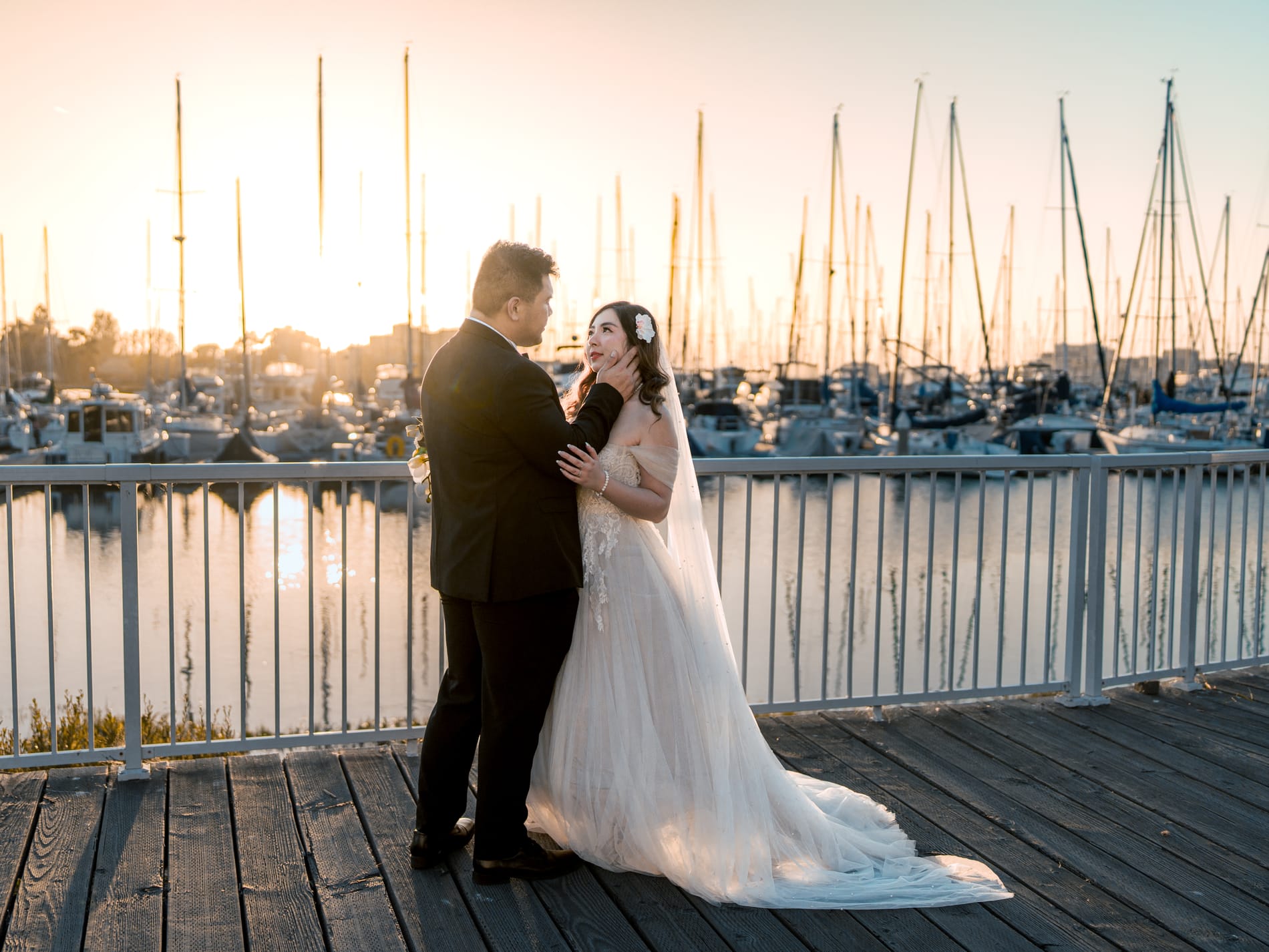 Bride and groom holding each other on the boardwalk at sunset, her train spread across the boards