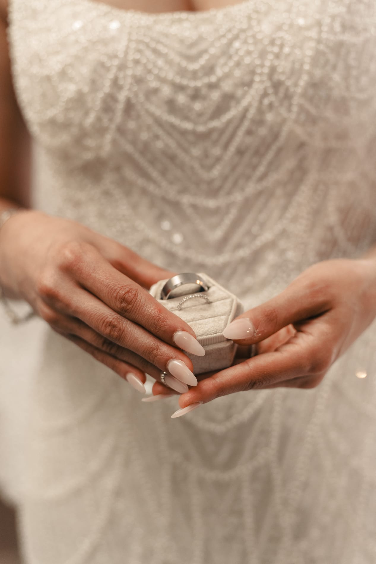 Bride holding the open ring box in both hands against her beaded gown