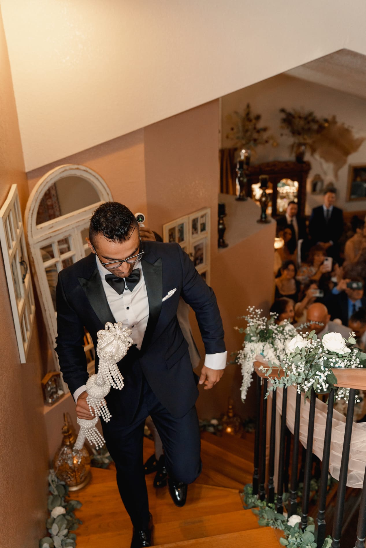 Groom climbing the staircase carrying the pearl ceremonial scepter, guests waiting below