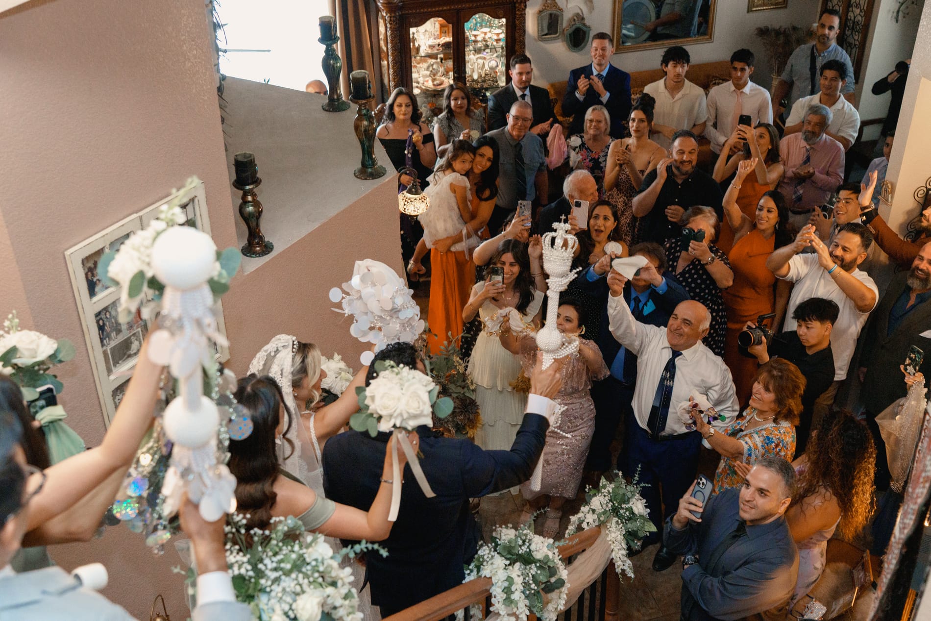 Guests raising pearl ornaments and cheering as the couple enters, seen from above