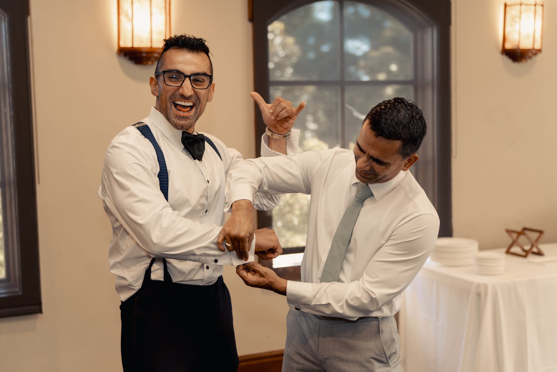 Groom laughing while a groomsman fastens his cufflink before the ceremony