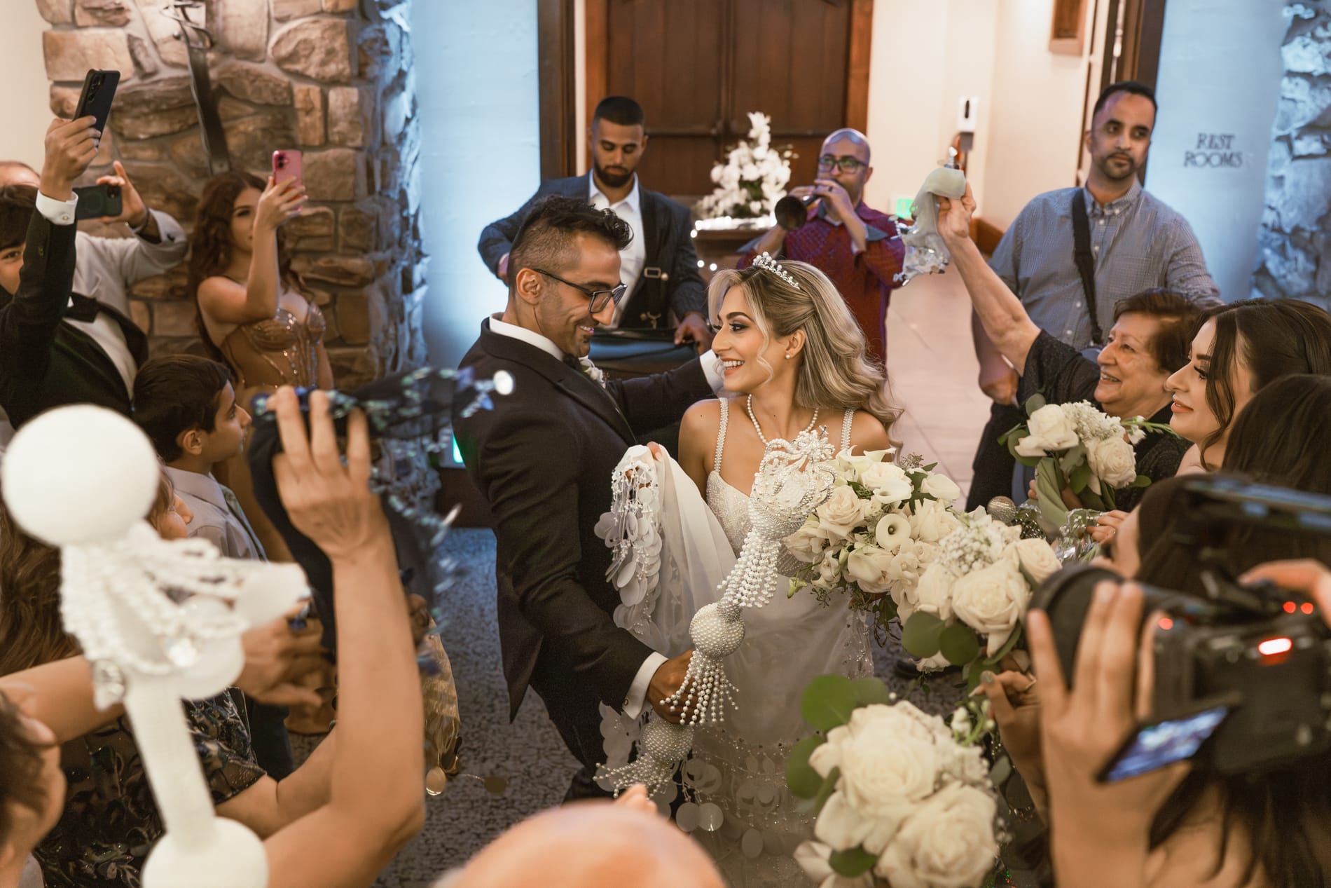 Bride and groom moving through a crowd of guests with phones and flowers raised