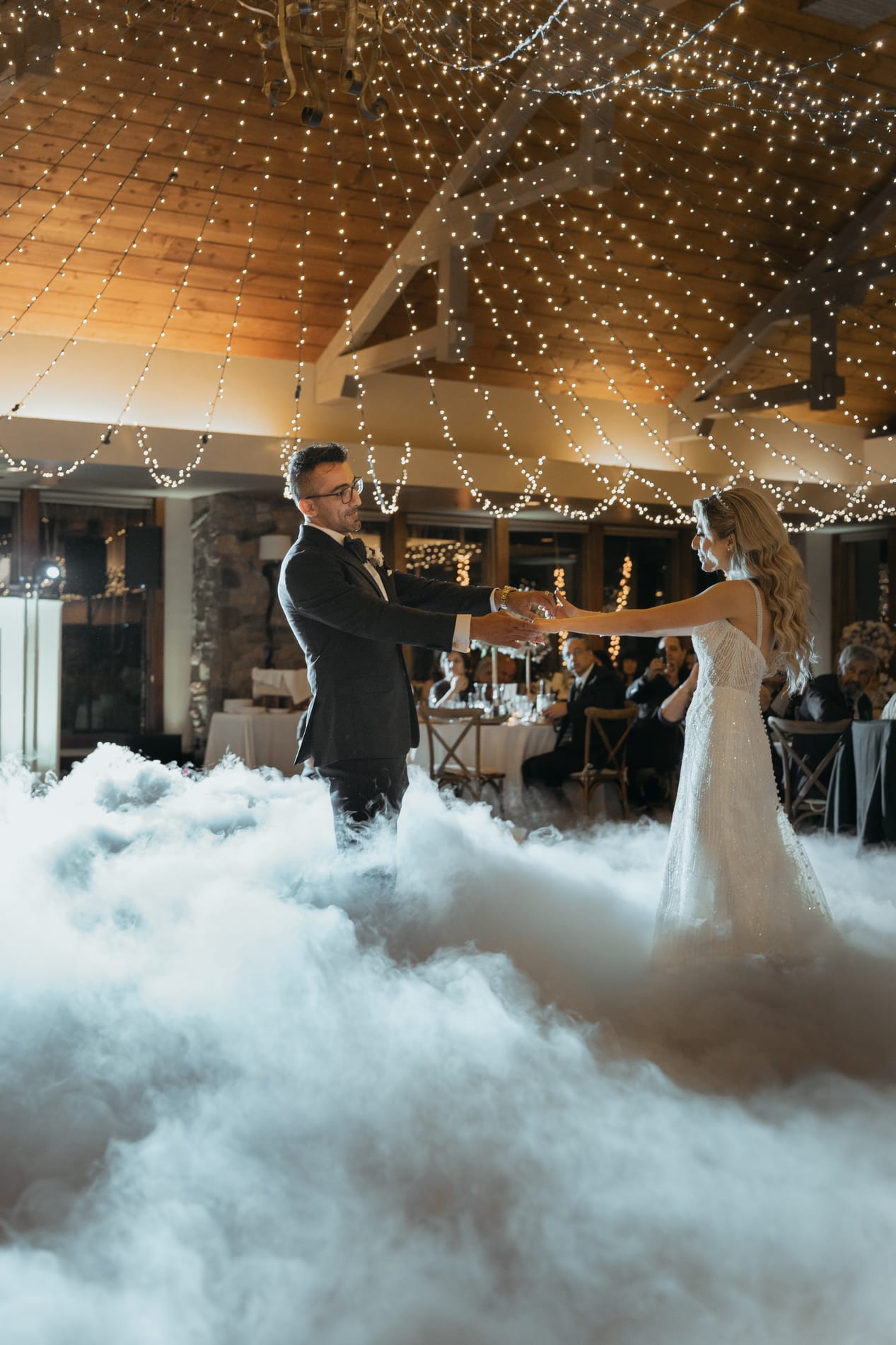Bride and groom reaching for each other across the fog at the start of their first dance