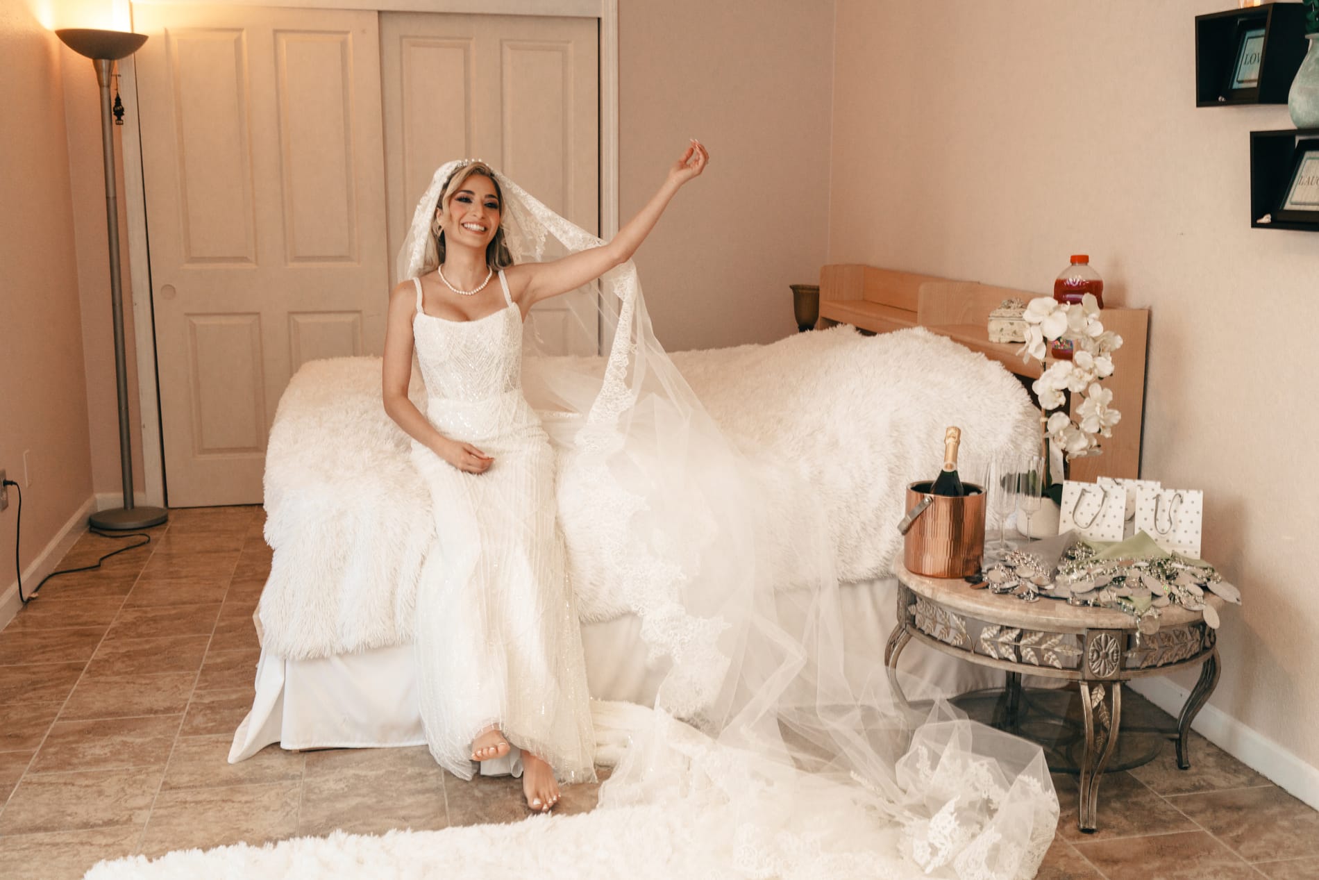 Bride sitting at the end of the bed in her gown and veil, champagne chilling on the side table