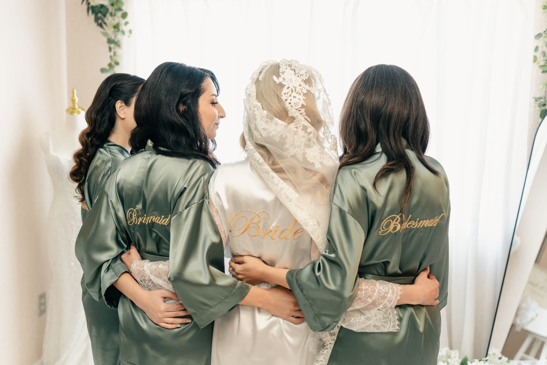Bride and her bridesmaids in matching robes, backs to the camera, arms around each other